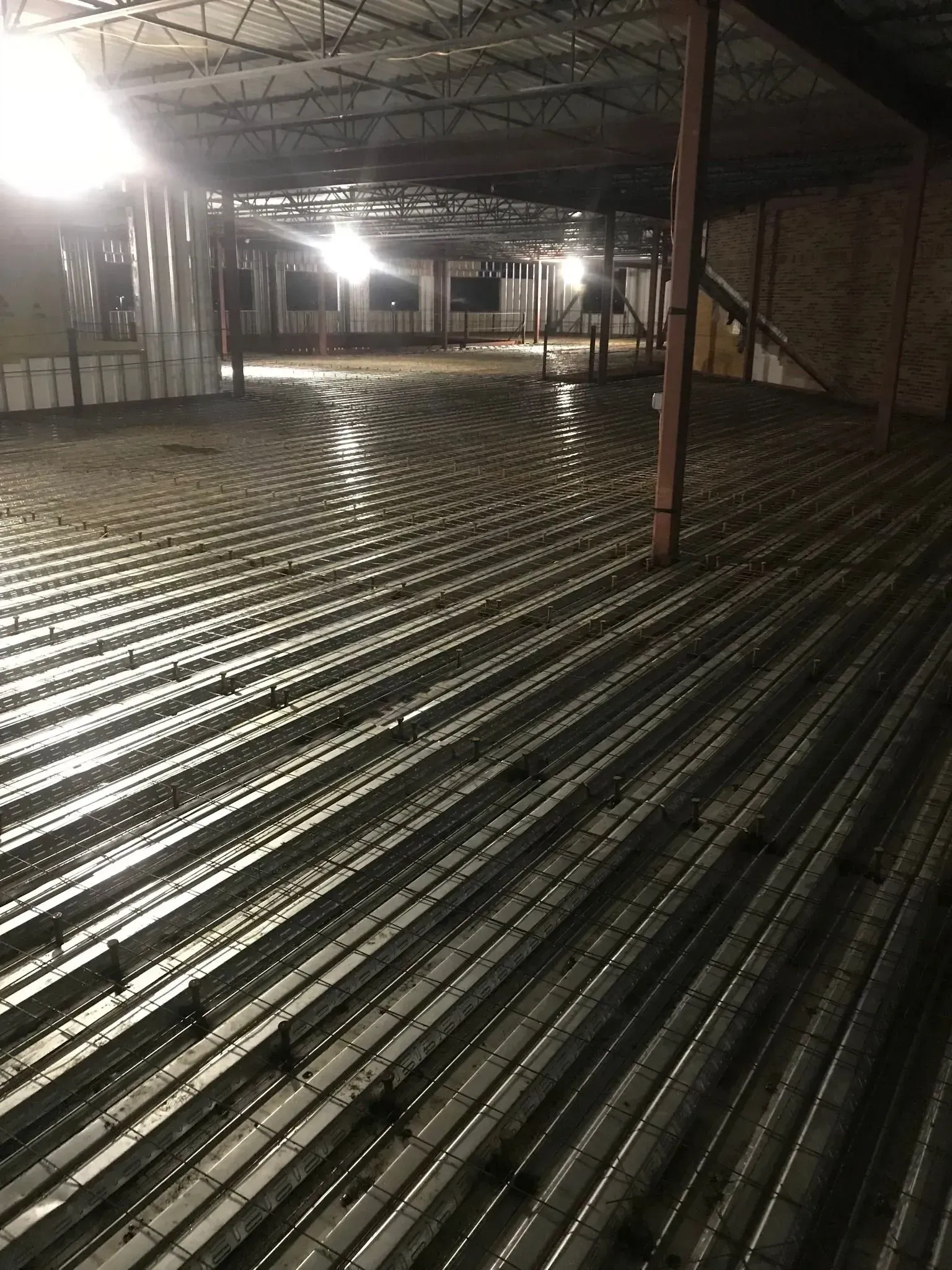 Interior of a building under construction. Metal decking and rebar cover the floor, dimly lit.