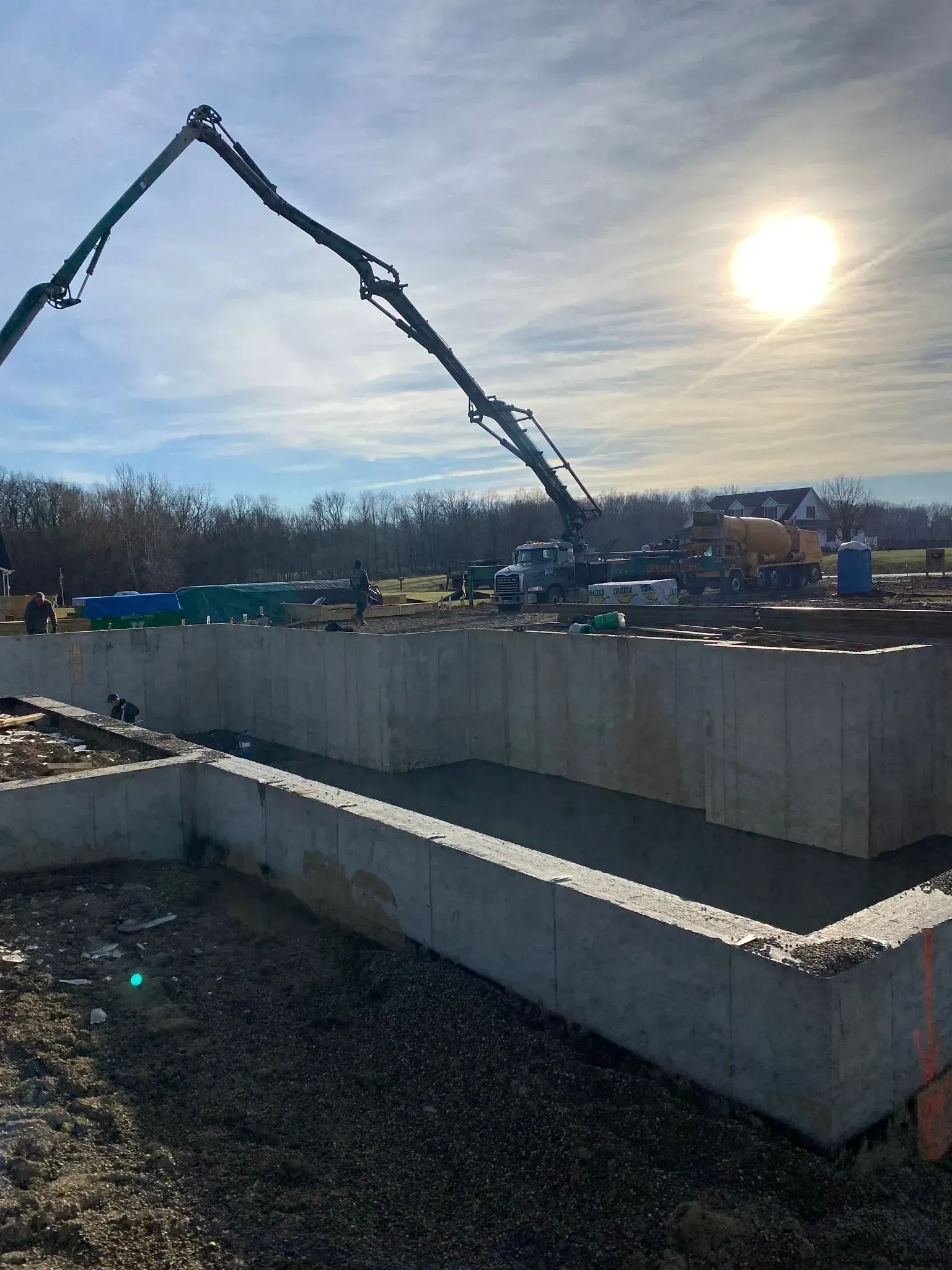 Concrete being poured into a foundation. A pump truck extends over the gray concrete walls, bright sun in the sky.