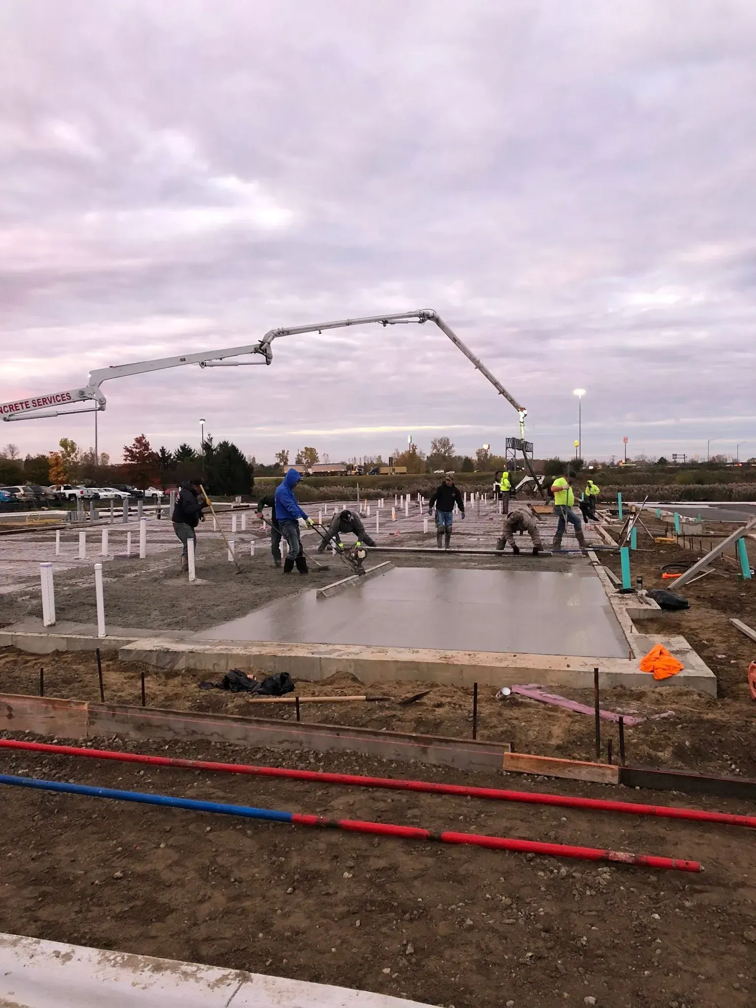 Construction workers pouring concrete at a construction site using a pump, cloudy sky overhead.
