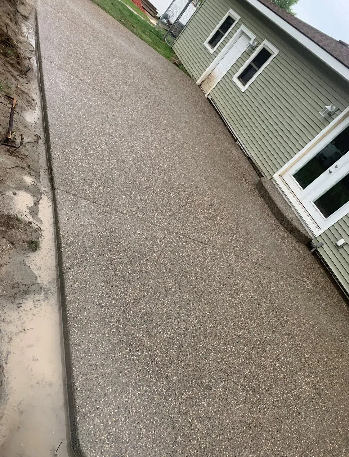 Concrete driveway next to a light green house with white trim.