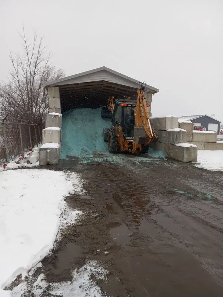Loader in a salt shed; blue salt pile, snow, concrete blocks, muddy road.