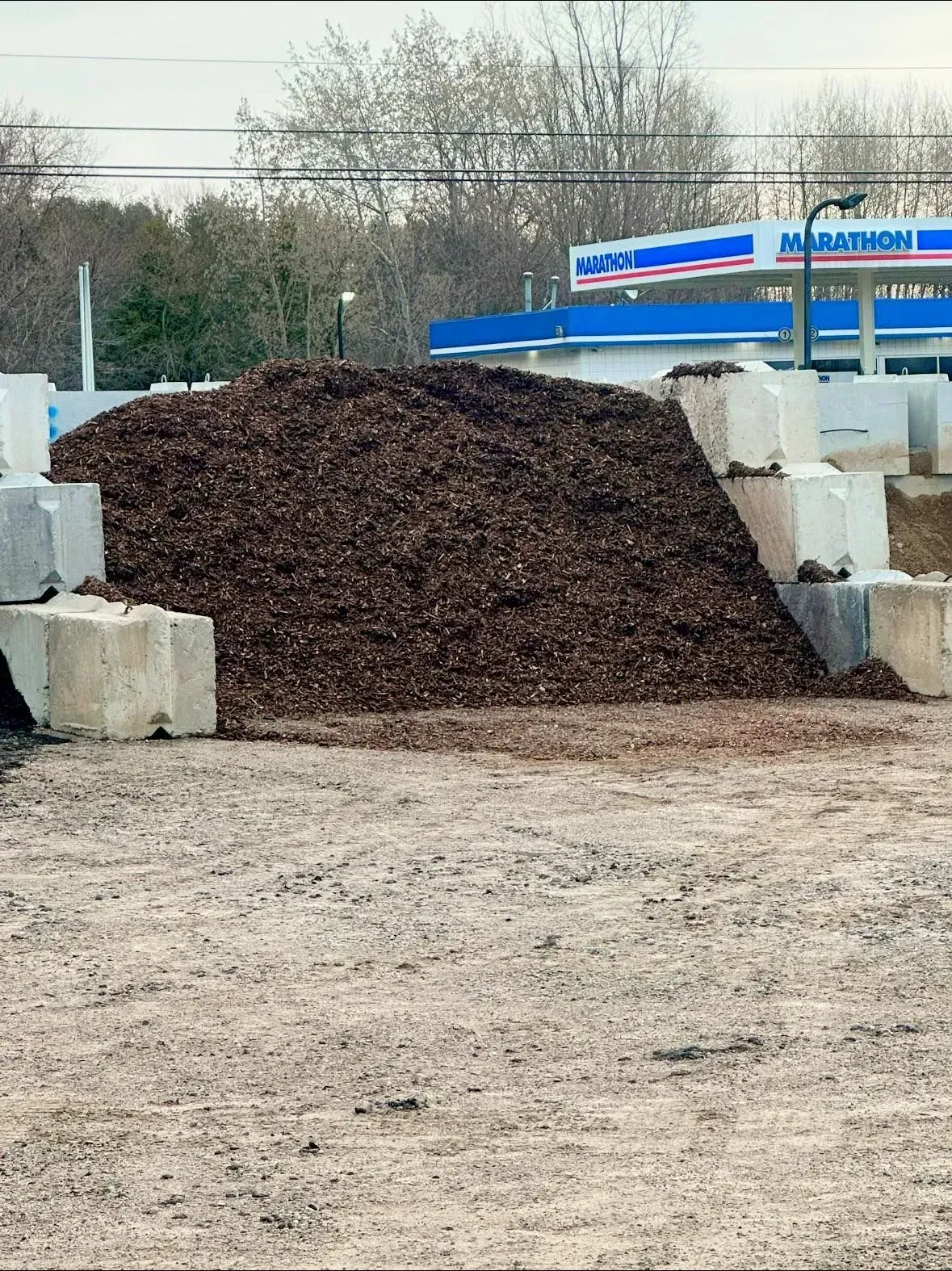 Pile of brown mulch bordered by concrete blocks, gas station in the background.
