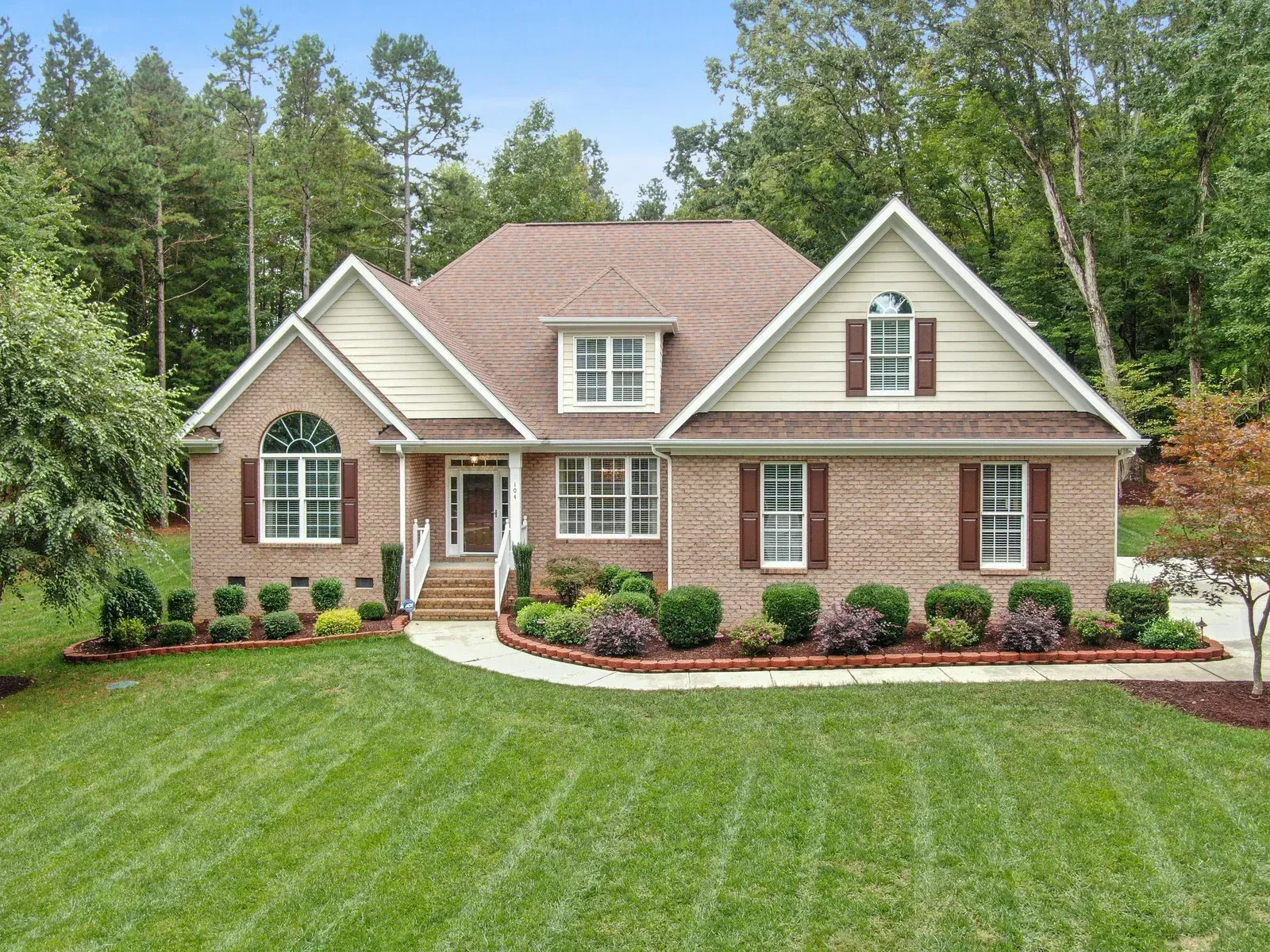 Brick house with a well-manicured lawn and landscaping in a wooded area.