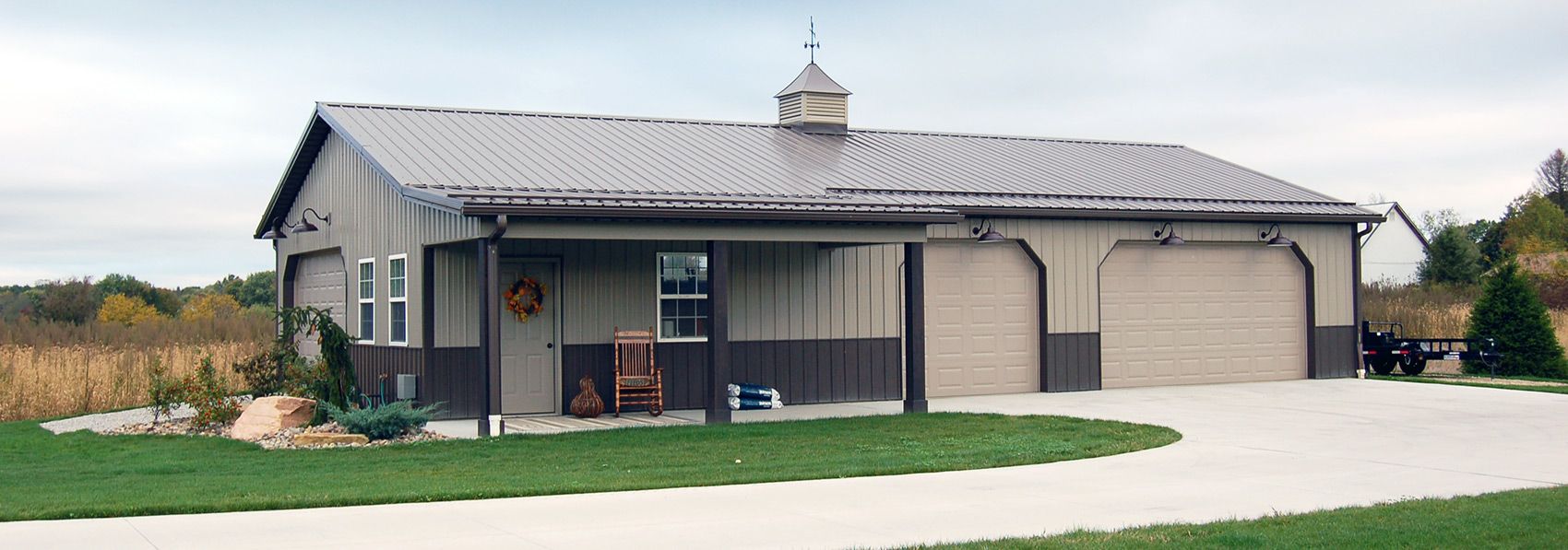 Red barn with white doors and a dark gray roof in a grassy field under a cloudy sky.