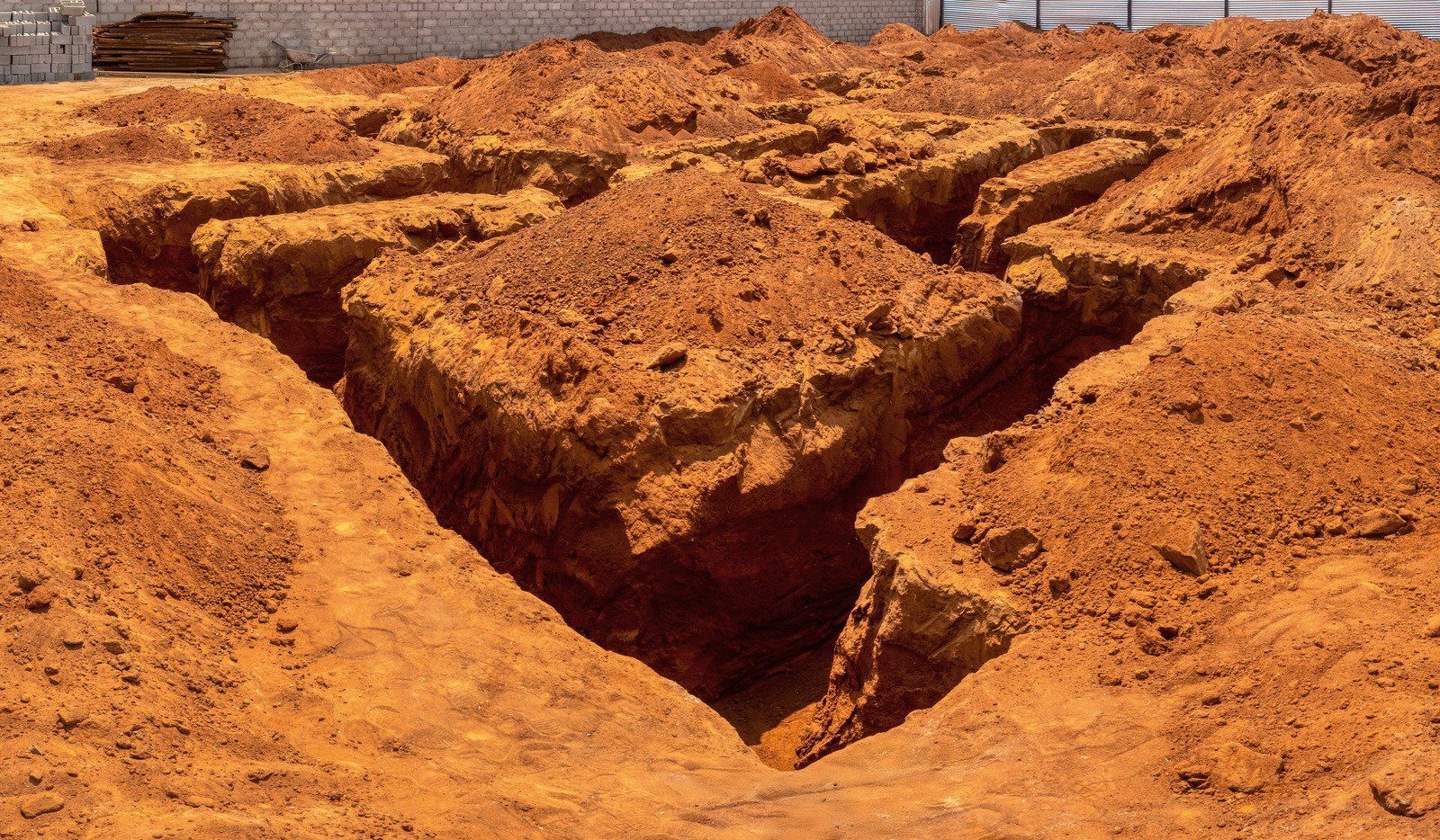 Excavated red earth foundation trenches, prepared for construction, outdoors.