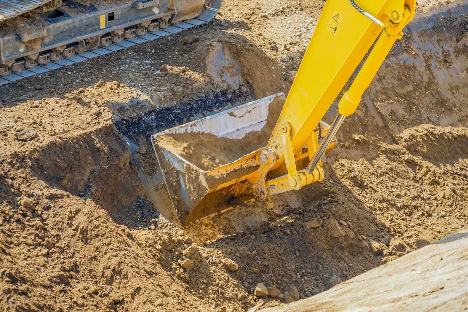 Yellow excavator bucket digging into brown dirt.