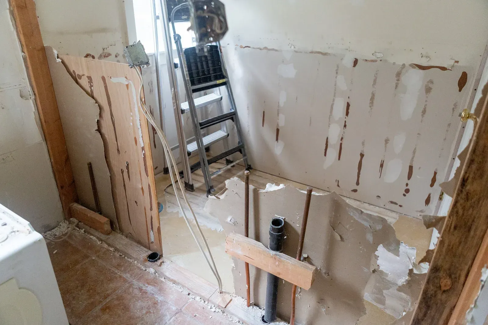 Bathroom renovation in progress, walls stripped to studs; ladder and equipment present.