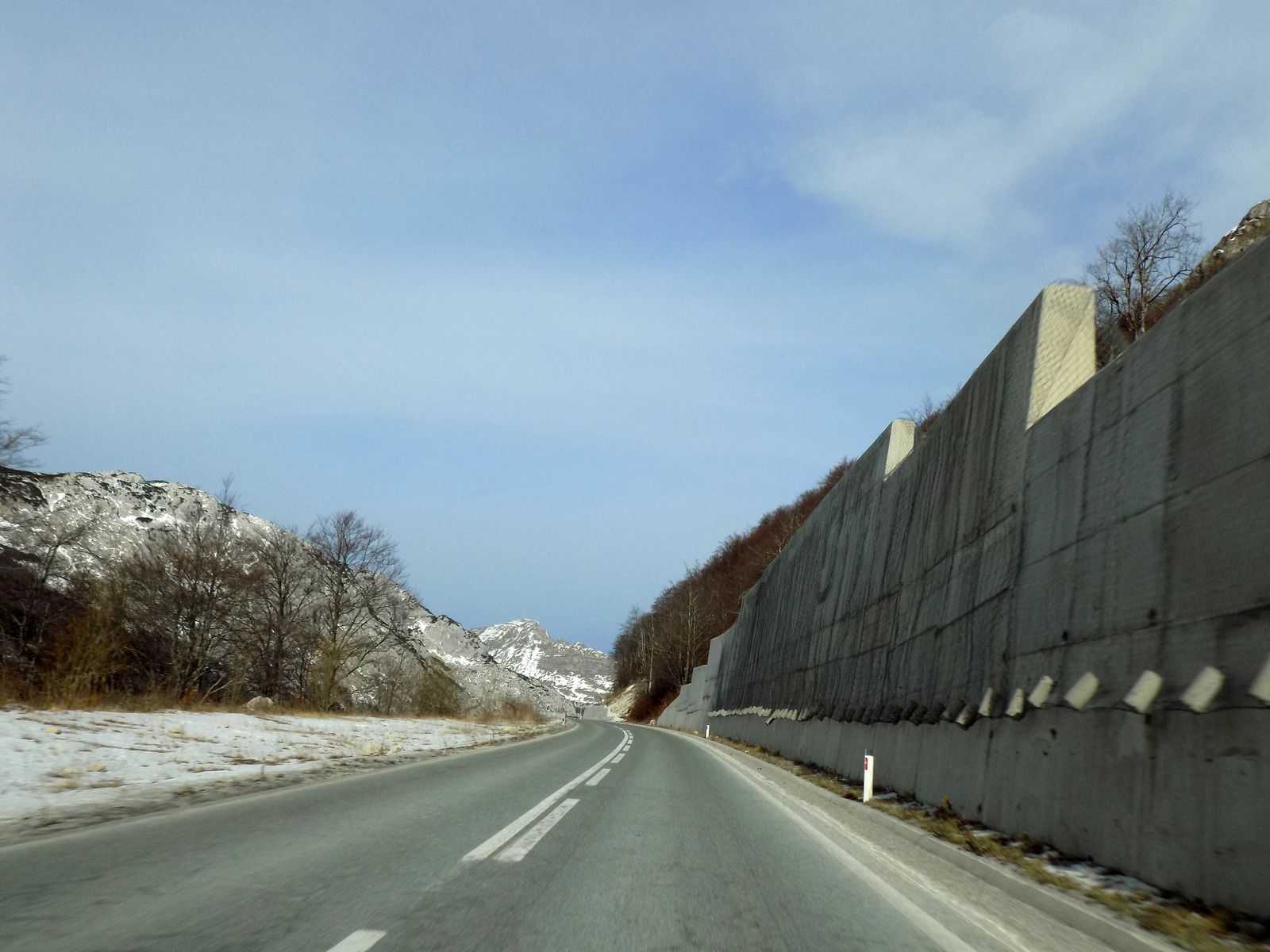 Highway through a snowy landscape, concrete retaining wall, blue sky.