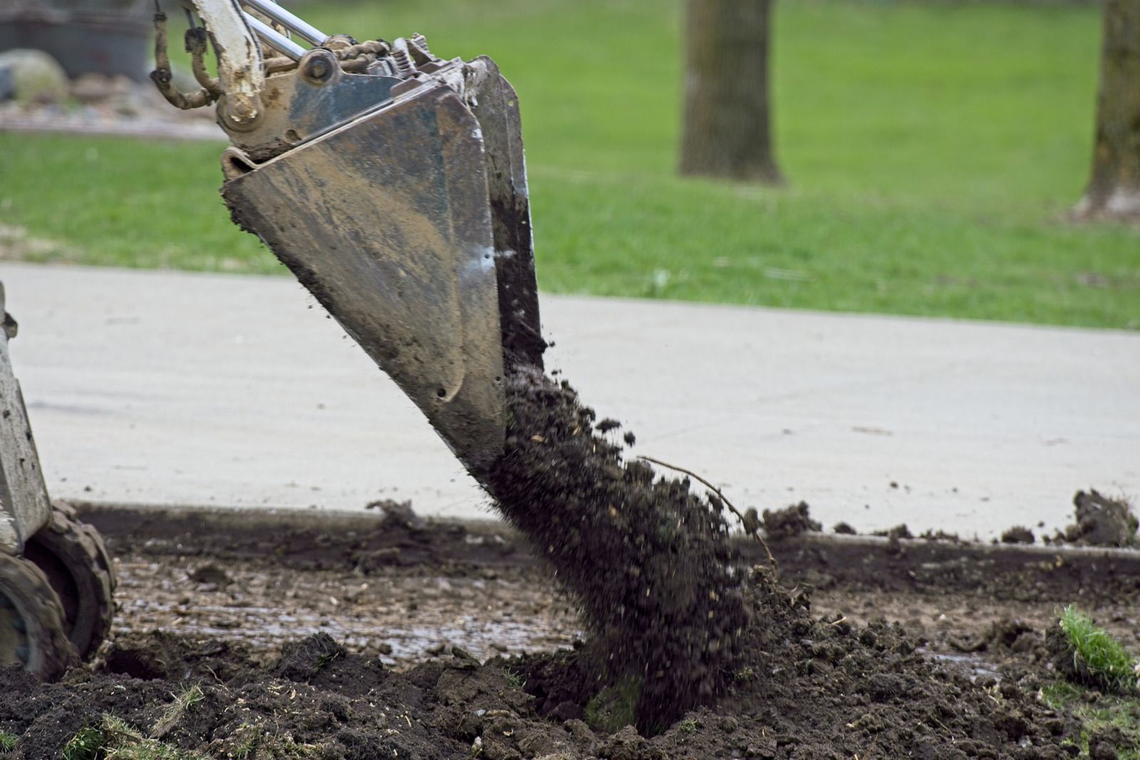 A small excavator bucket dumping dirt onto the ground.