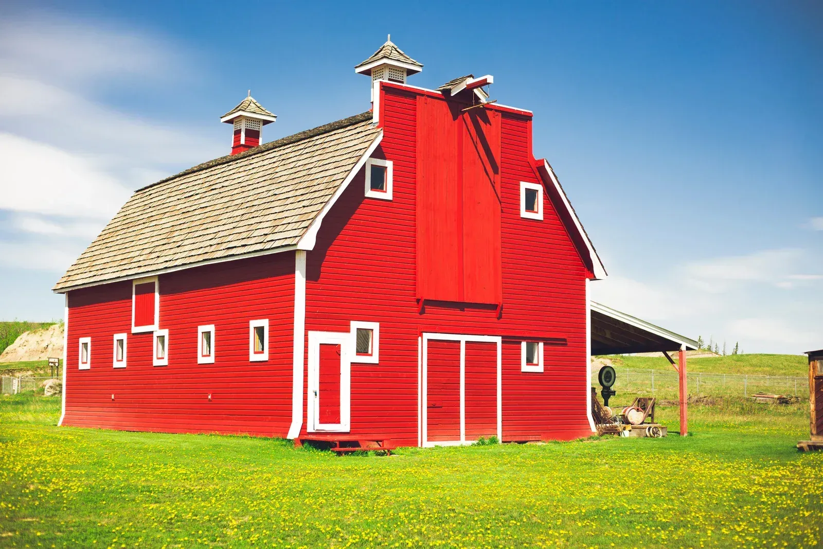 Red barn with white trim, tan roof, chimney, and green grass. Blue sky.