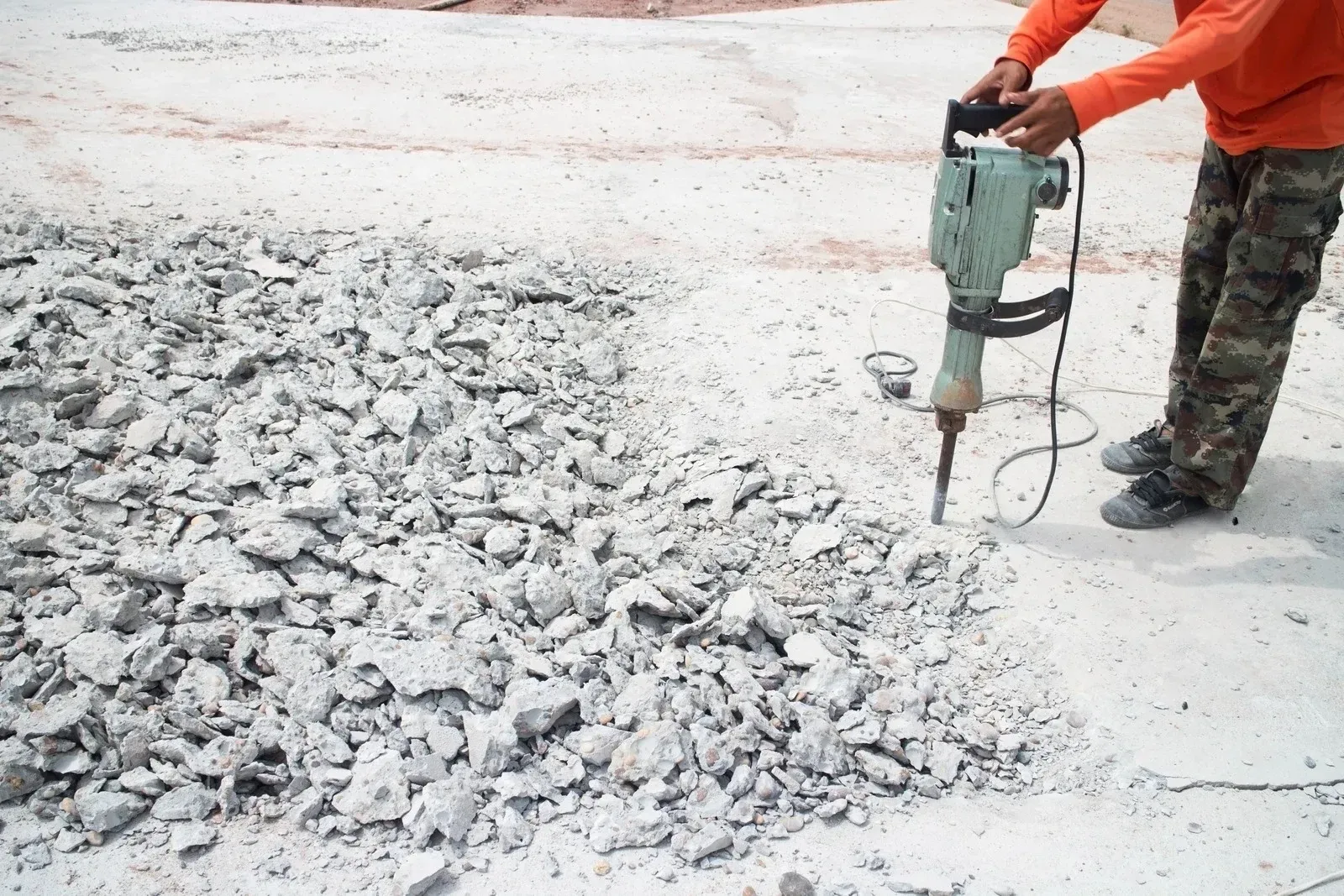 Man using a jackhammer to break up concrete on a construction site.