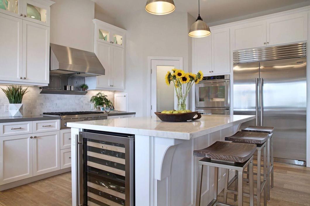 A kitchen with white cabinets , stainless steel appliances , a large island and a wine cooler.