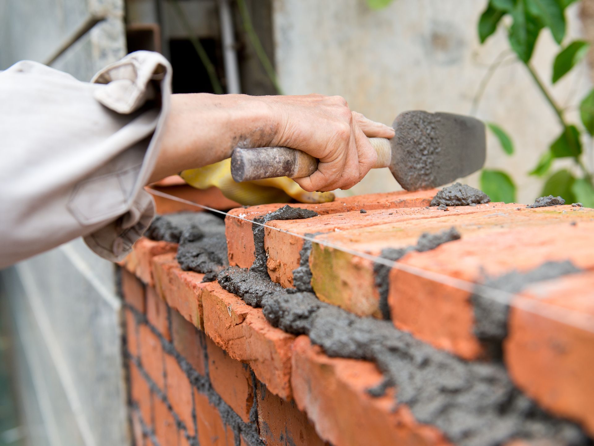 A person uses a trowel to apply mortar to a row of orange bricks while building a wall.