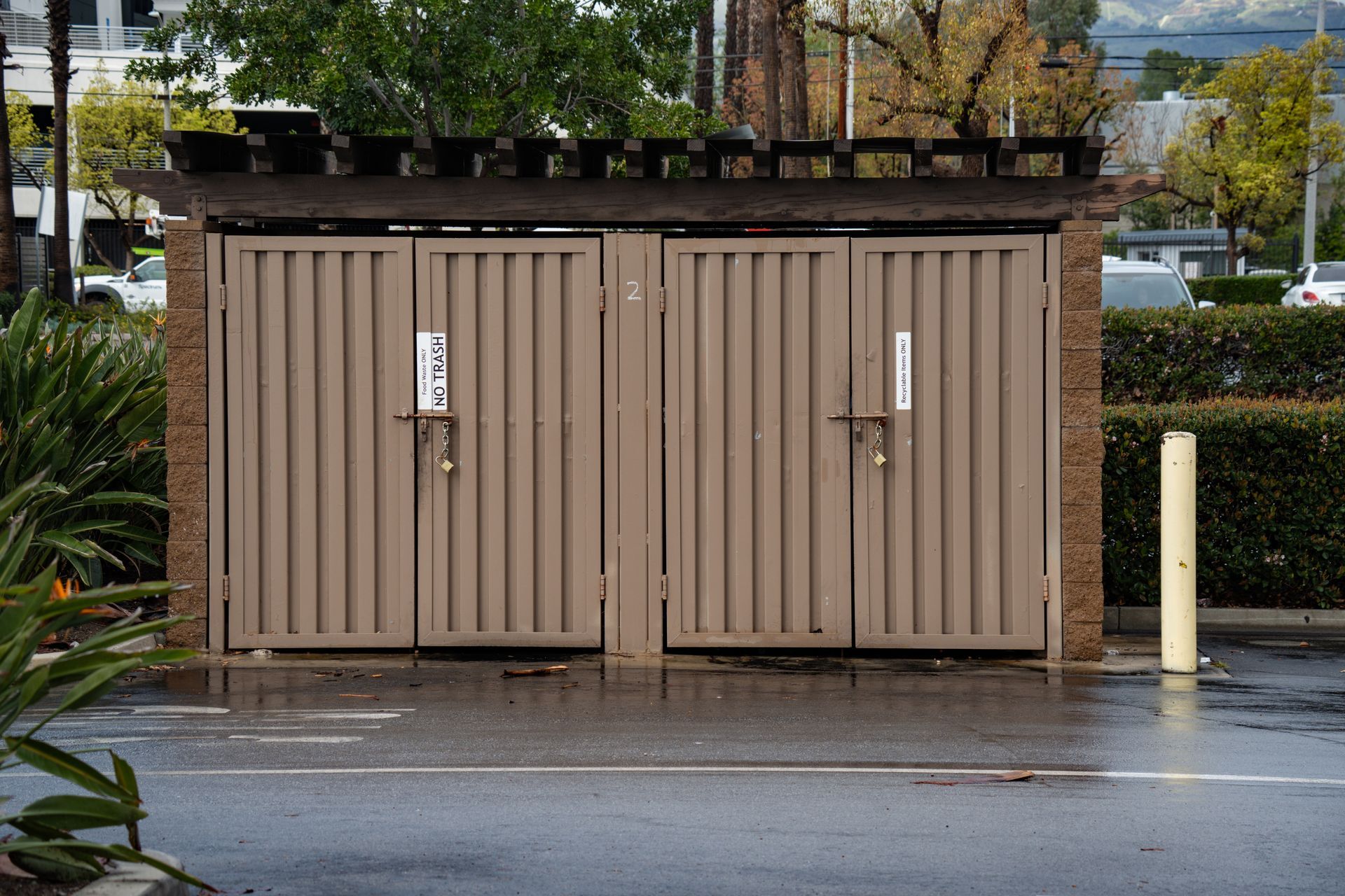 A brown, fenced trash enclosure with two sets of double doors.