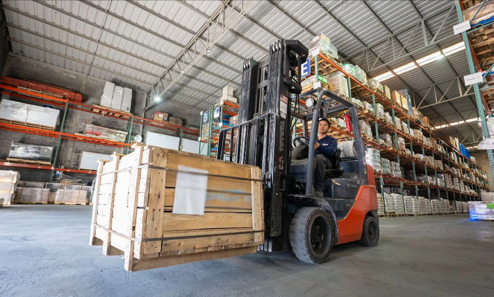 Operador montacargas transportando caja de madera en almacén industrial con estanterías de productos a gran escala