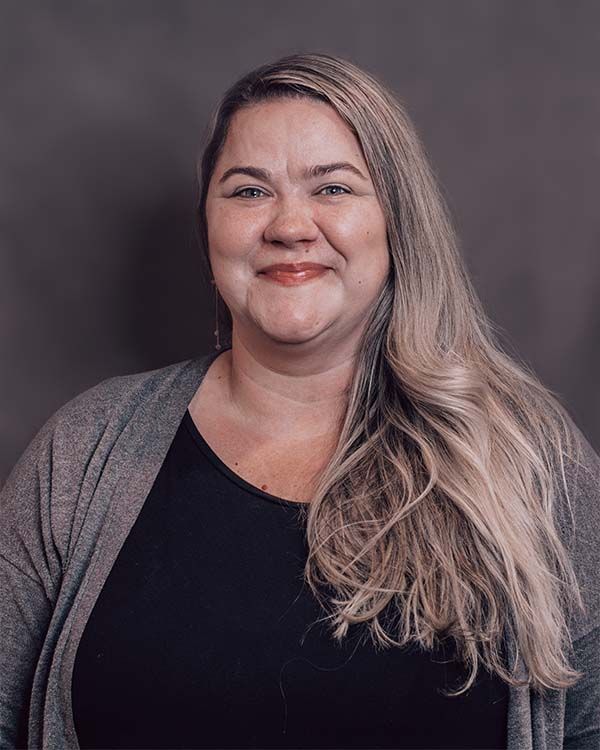 A woman with long blonde hair is wearing a black shirt and a gray cardigan.
