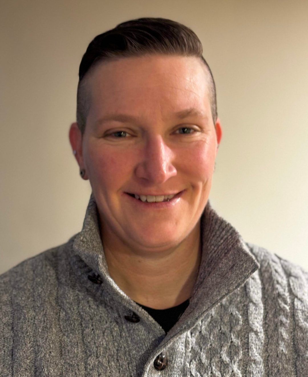 A woman wearing a grey sweater is smiling for the camera