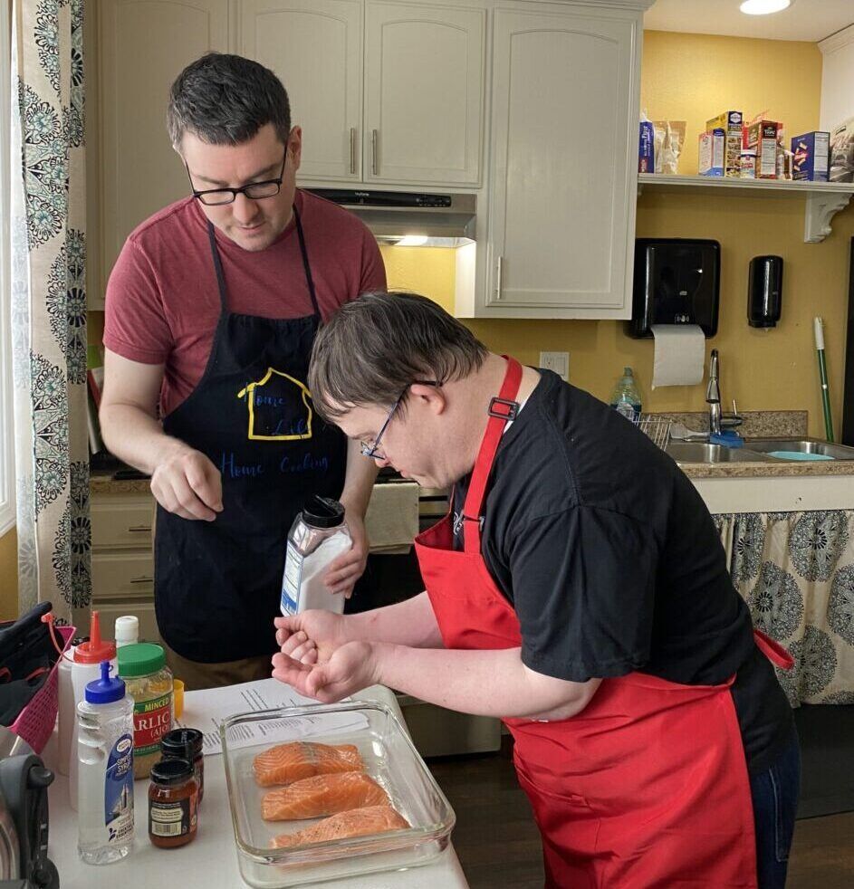 Two men in aprons are preparing food in a kitchen