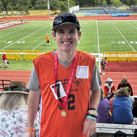 A man wearing a medal around his neck is standing in front of a football field.