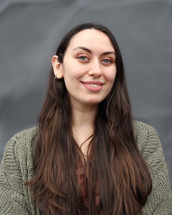 A woman with long hair is smiling and wearing a green sweater.