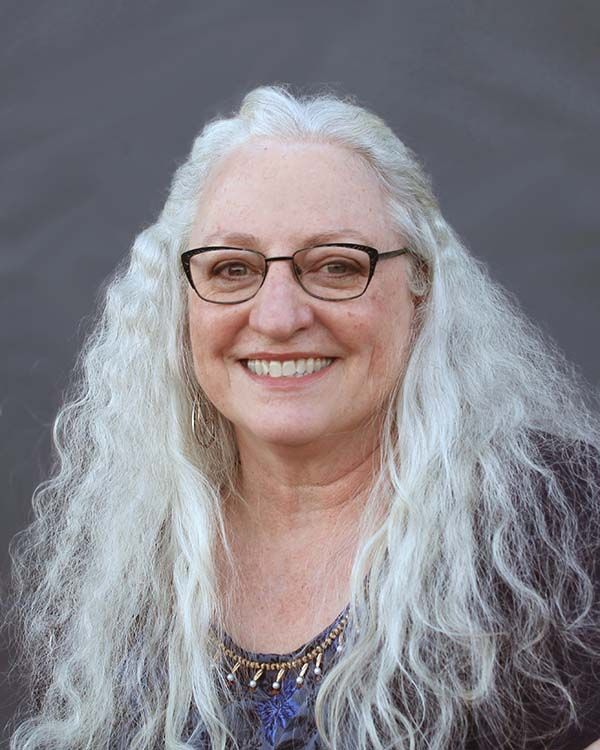A woman with long white hair and glasses is smiling for the camera.