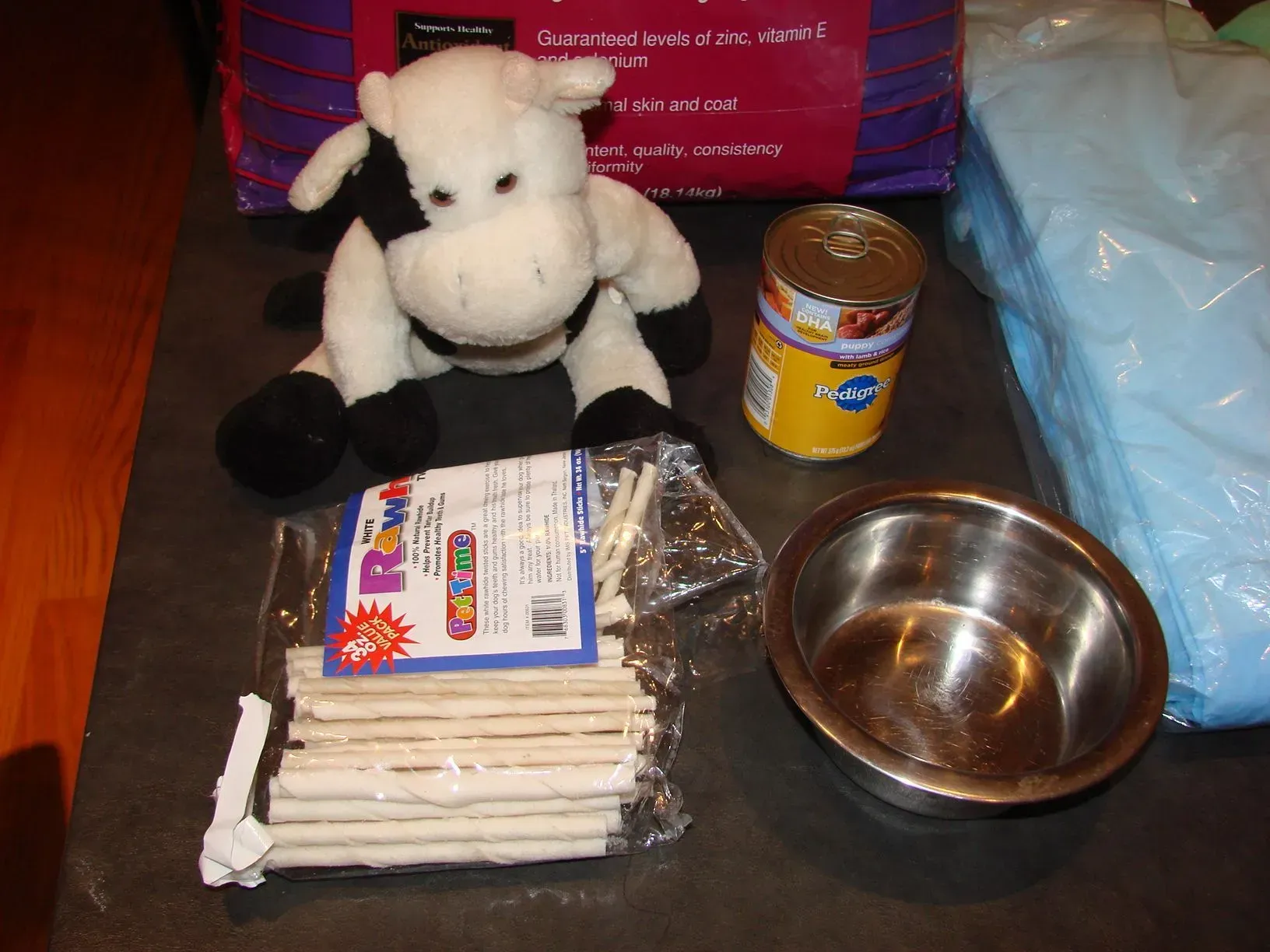 A stuffed cow sits on a table next to a can of food and a bowl