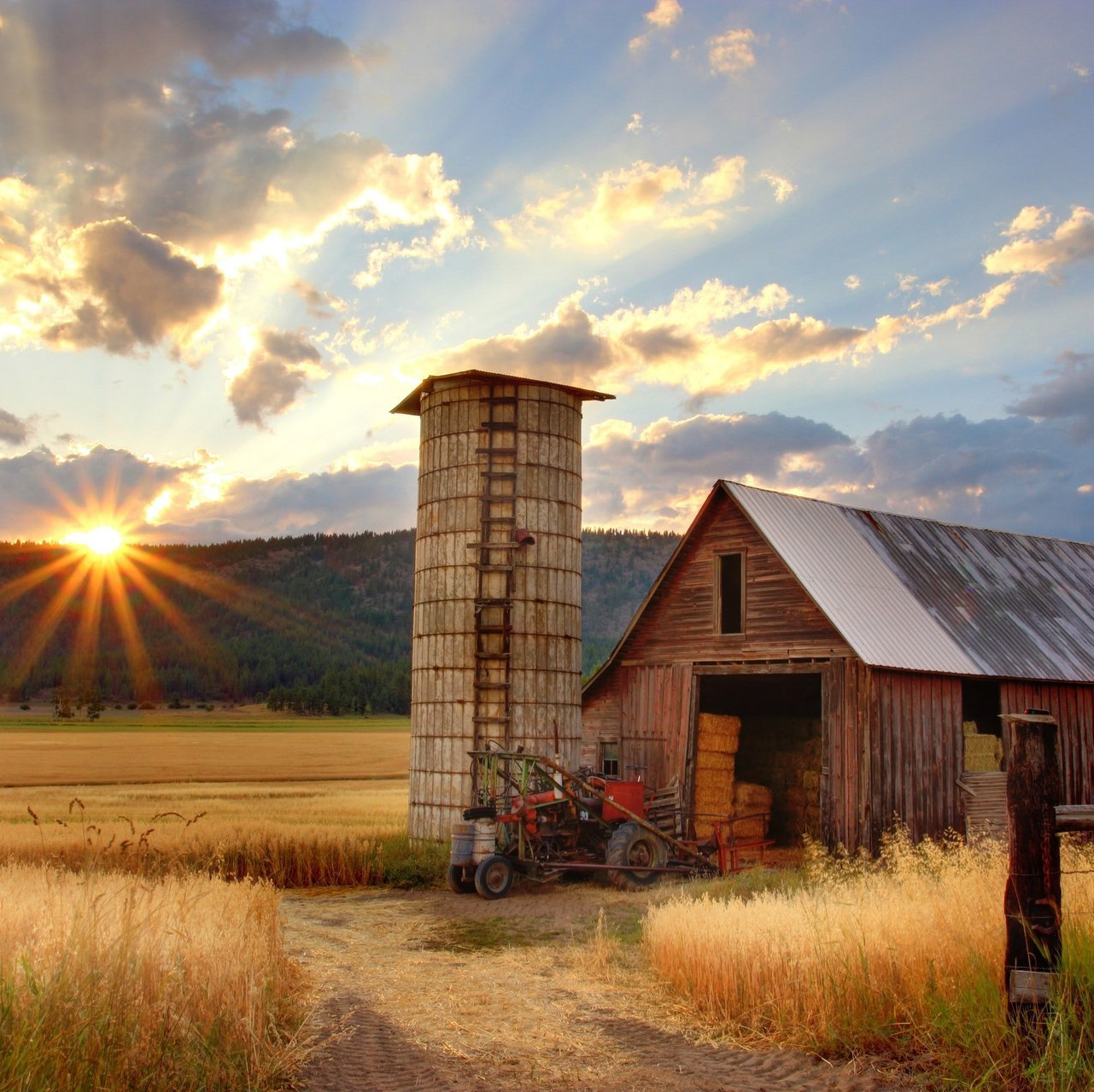 the sun is setting behind a barn and silo