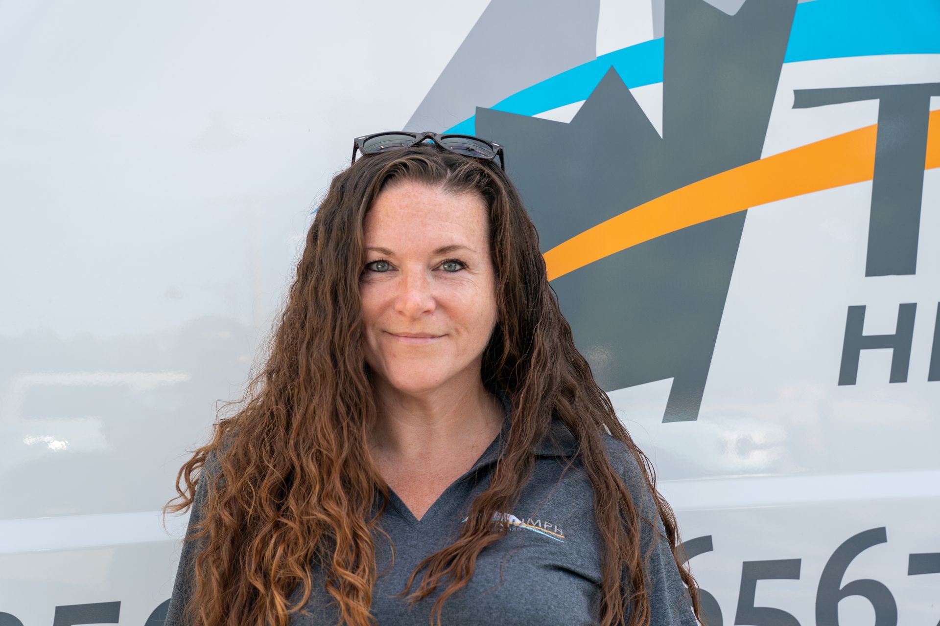 A woman with long curly hair is standing in front of a white van.