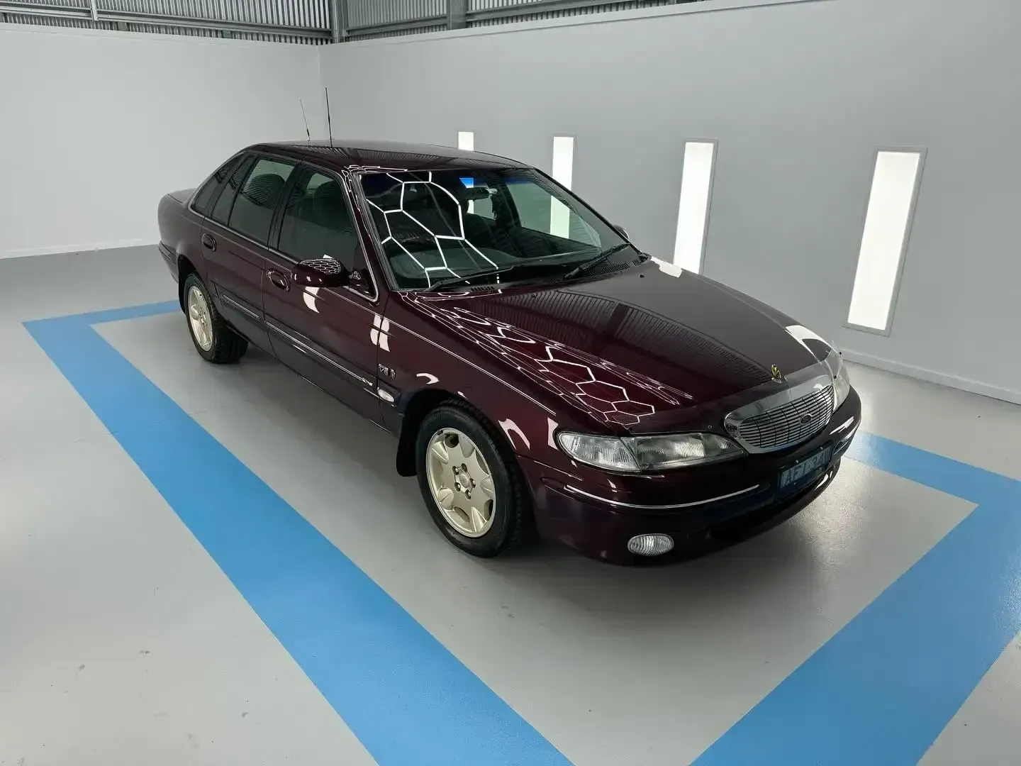 A Burgundy Car is Parked in a Garage With a Blue Stripe on the Floor — Bathurst Detailing Studio in Bathurst, NSW
