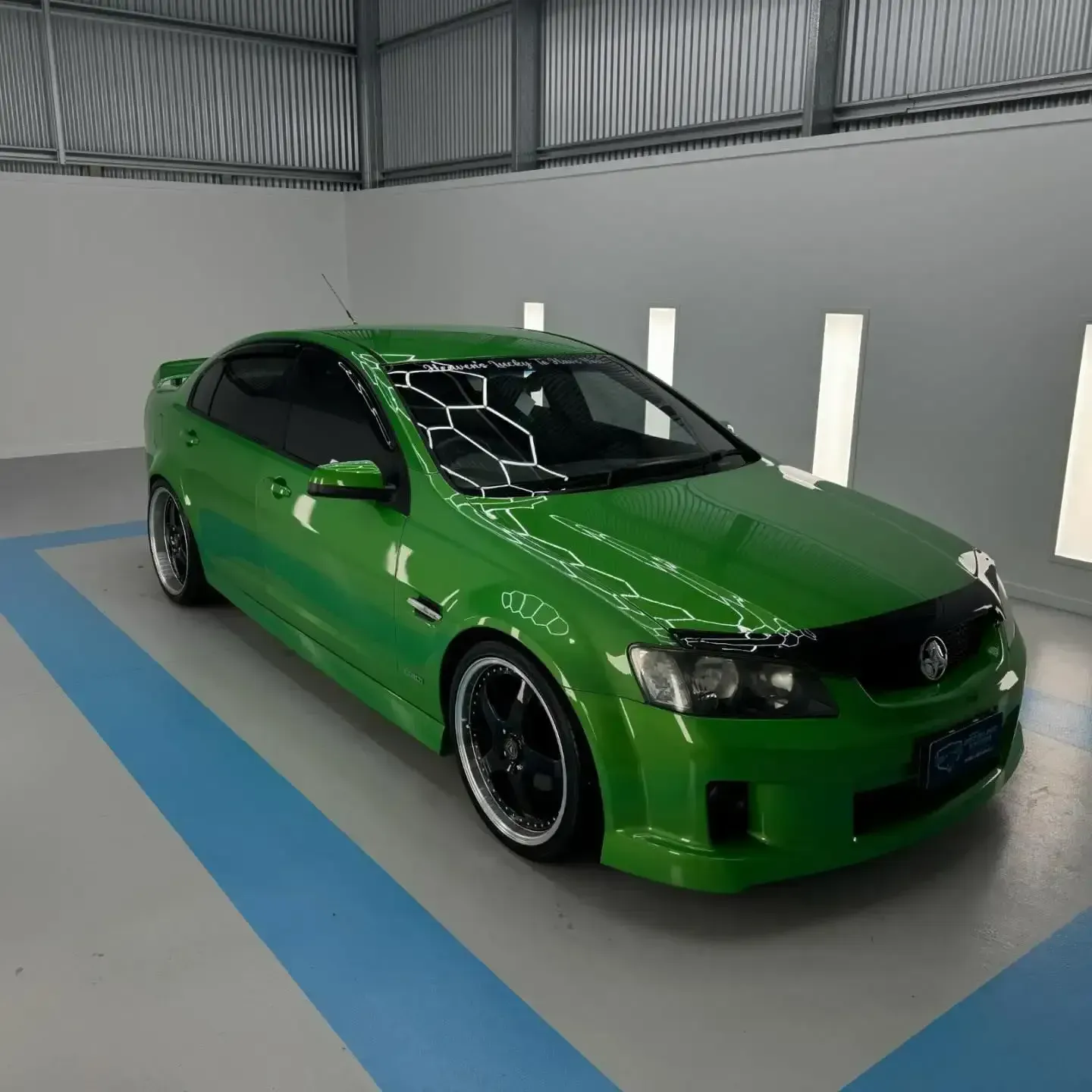 A Green Car is Parked in a Garage With a Blue Stripe on the Floor — Bathurst Detailing Studio in Bathurst, NSW