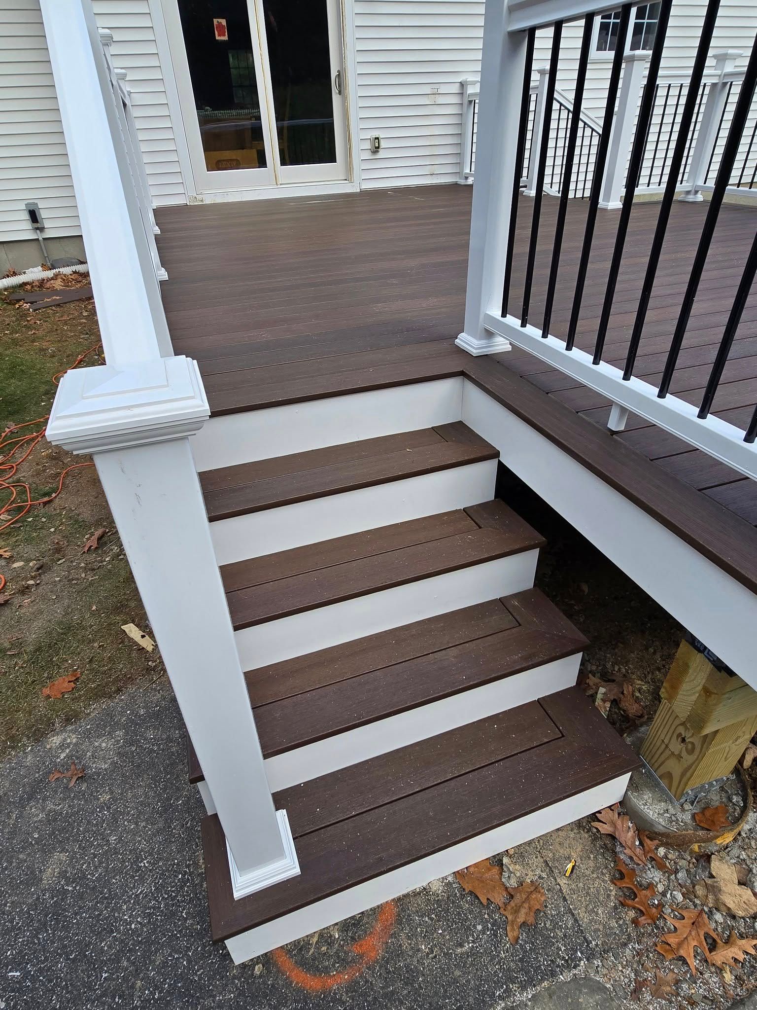Outdoor deck with dark brown steps and railing. White posts and trim contrast the dark wood.