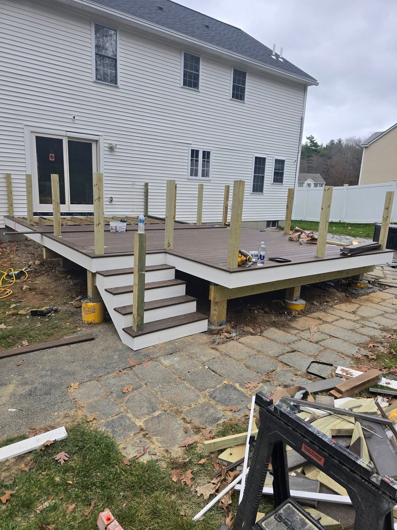 Deck under construction with stairs leading to a backyard. Brown decking and white trim, wooden posts.