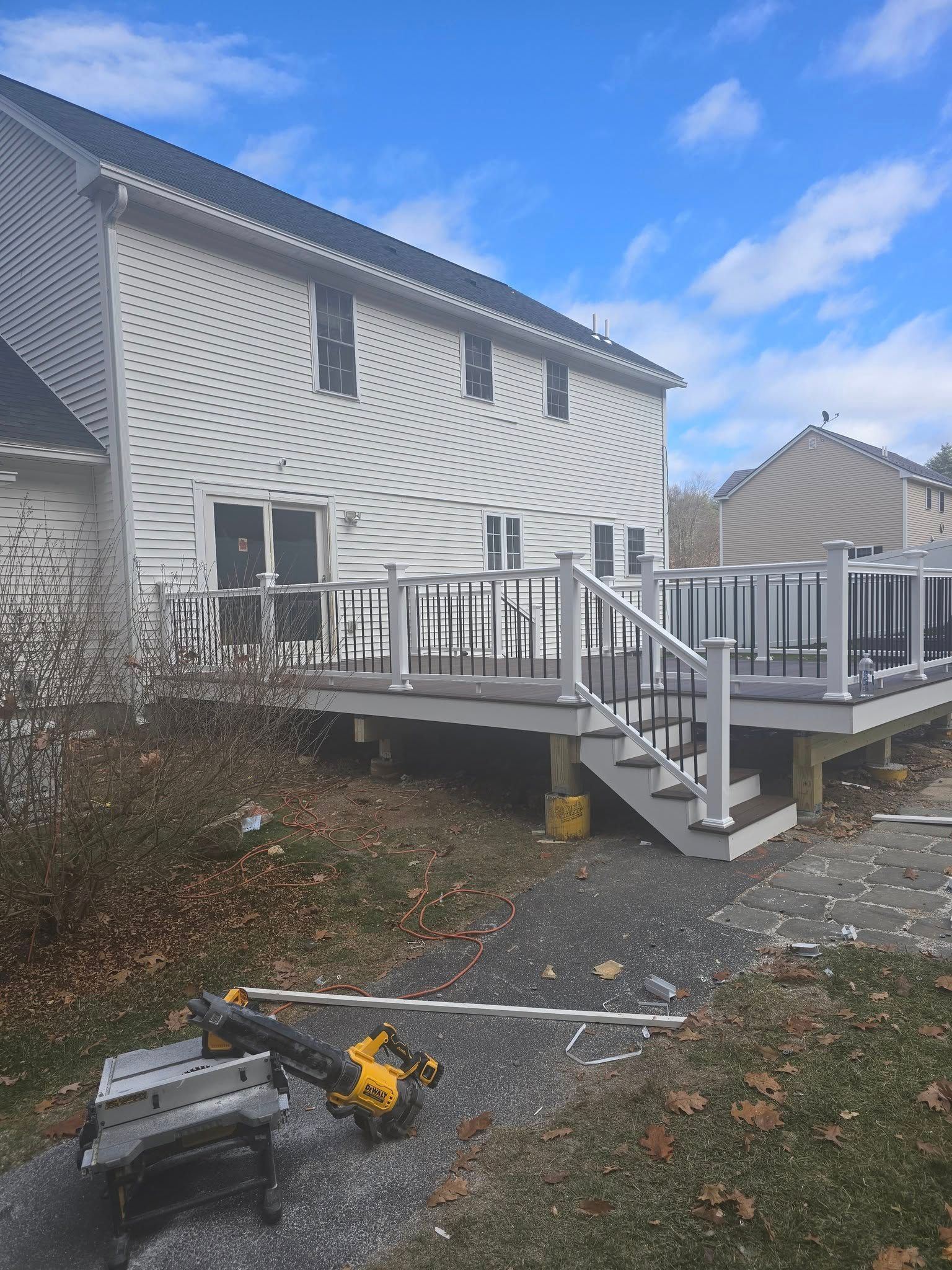 Back of house with new gray deck and black railing. Power tools in foreground.