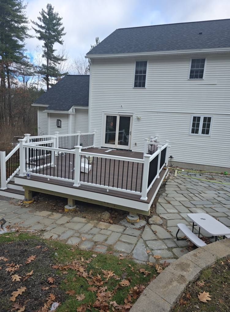 A two-story white house with a brown deck, white railing, and stone patio.