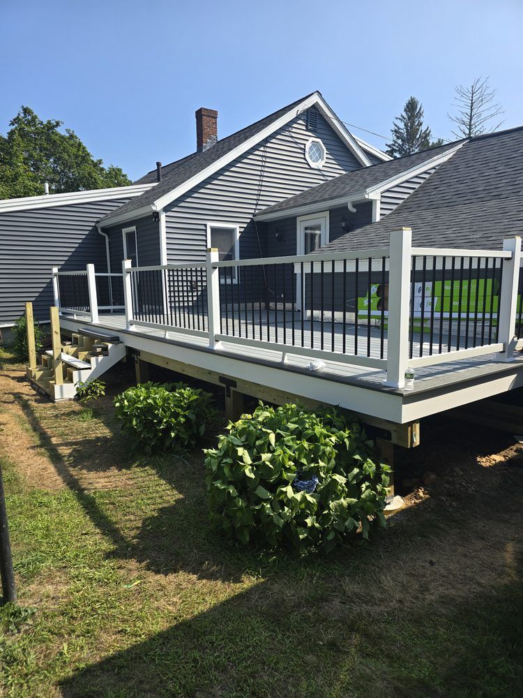 Deck with white railing and black spindles attached to a gray house, bushes underneath.