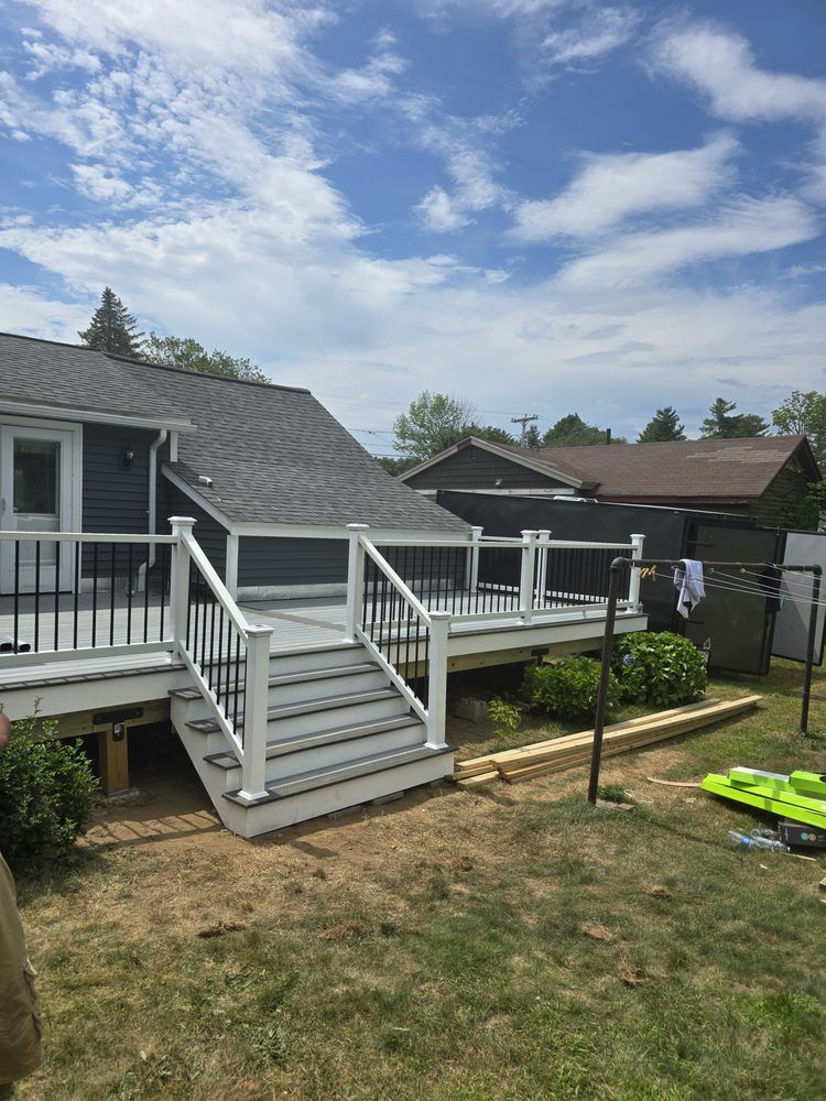 Backyard deck with gray siding, white railings, and steps, against a blue sky with clouds.