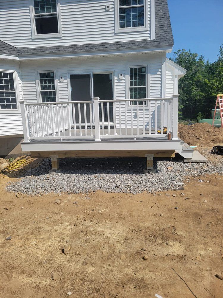 White deck with light gray decking and railing, with gravel base, next to a white house with windows.