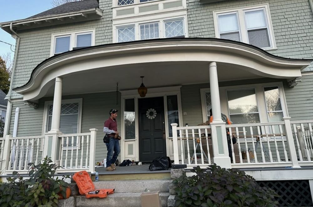Two-story house with curved porch, two people stand near the front door.
