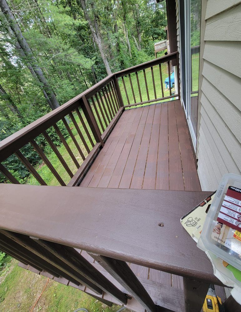 Brown wooden deck with railings, overlooking a green wooded area.