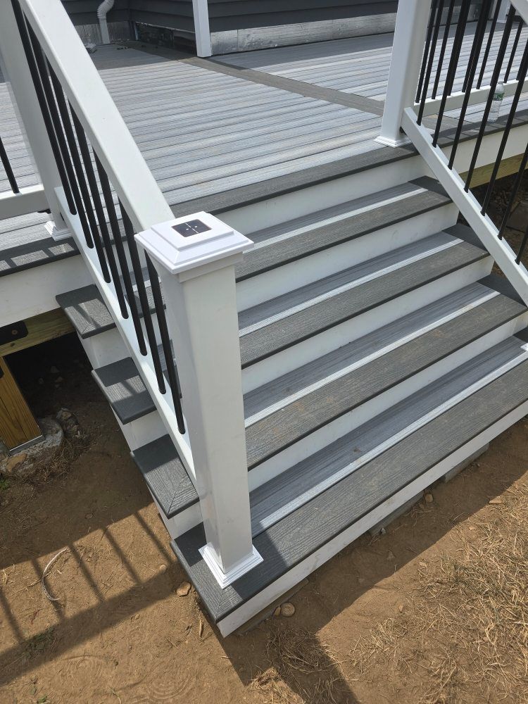 Grey and white deck with stairs and black railings leading down to dirt.