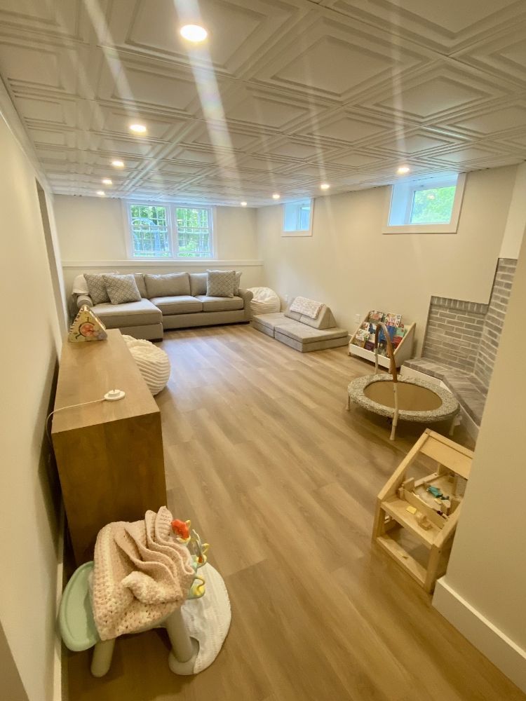 Playroom with sectional sofa, toys, and light wood flooring under a decorative ceiling.
