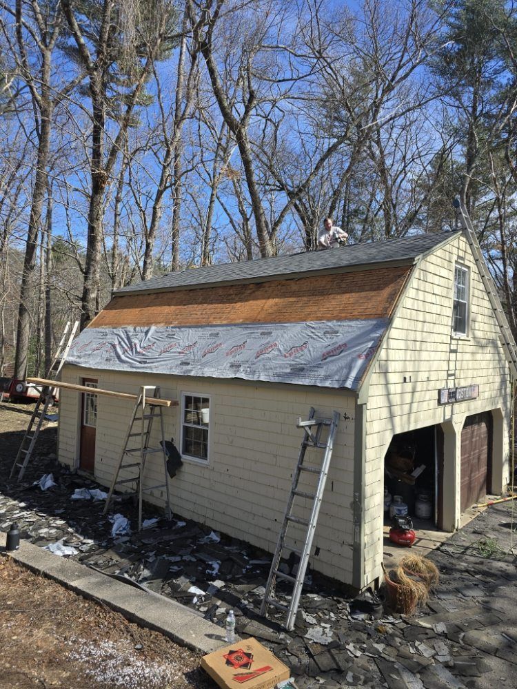 Garage under construction with new roofing. Person on the roof. Beige building, trees, and ladders visible.