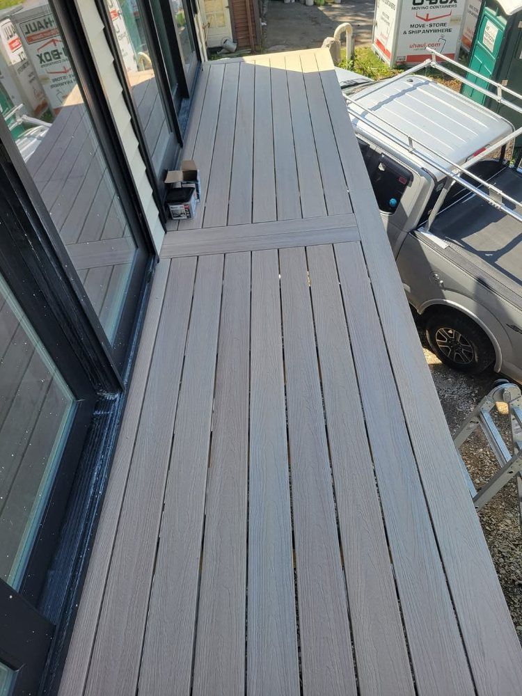 Grey composite decking on a raised platform, next to a window and a van.