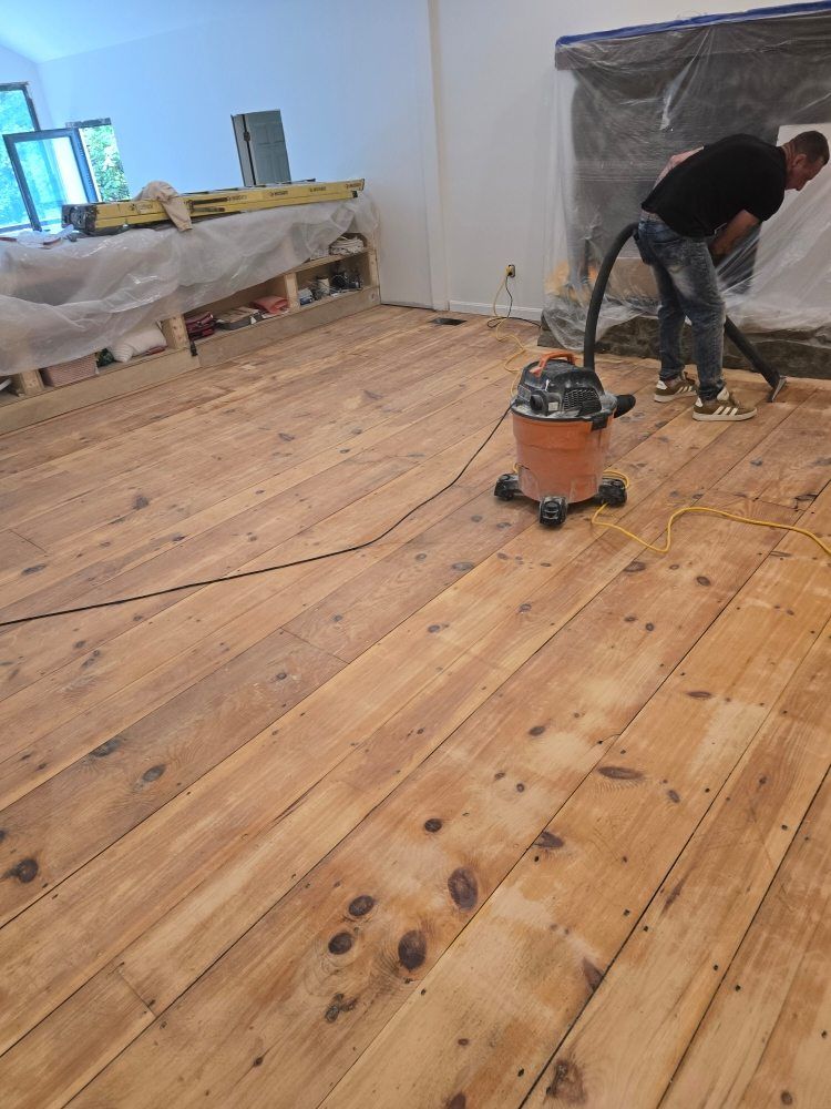 Man vacuuming a freshly sanded wooden floor in a room under renovation.
