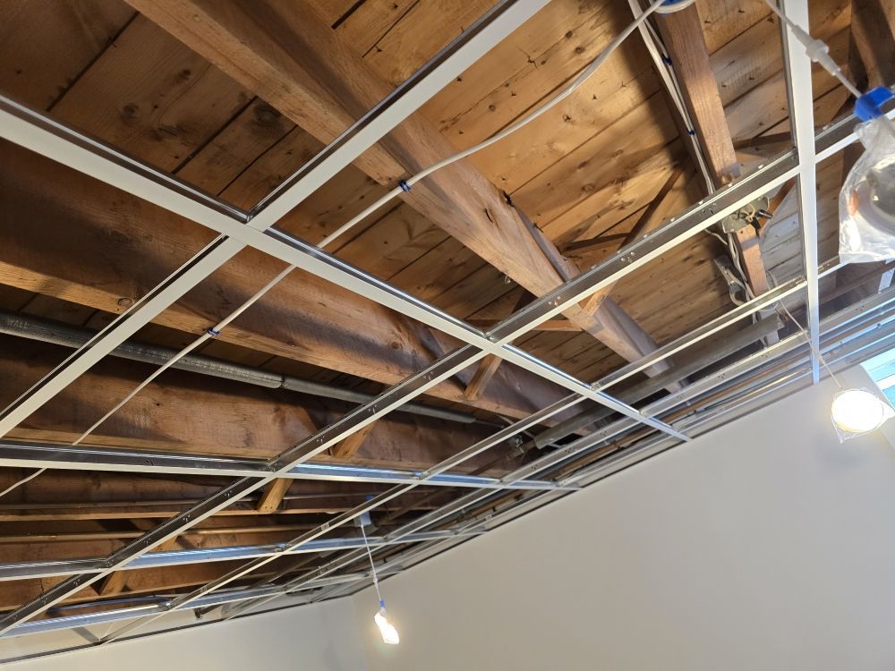 Metal grid suspended from a wood beam ceiling, likely for a drop ceiling.