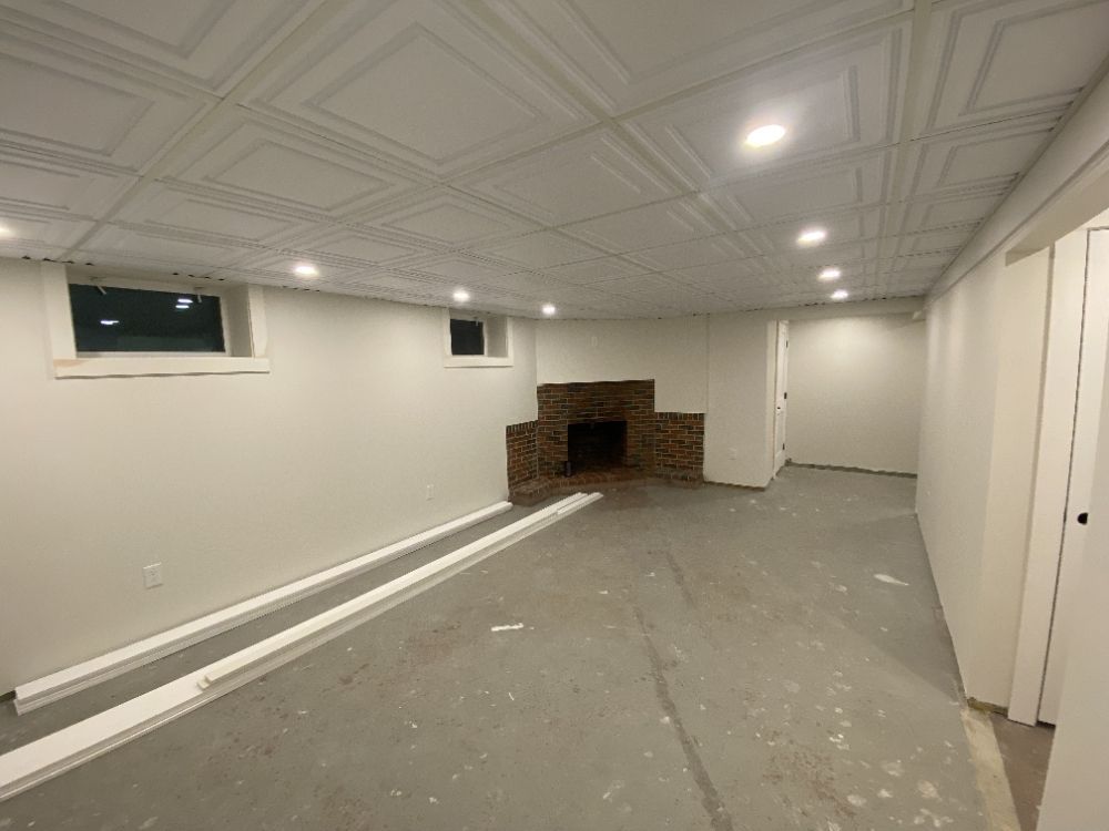 Basement with tiled ceiling, fireplace, two windows, recessed lighting, and white walls.