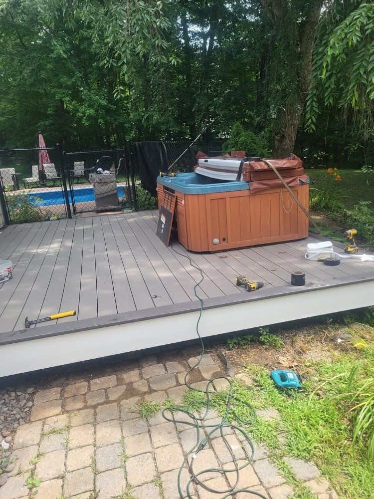 Hot tub on a grey deck with tools scattered nearby. In the background is a pool and trees.