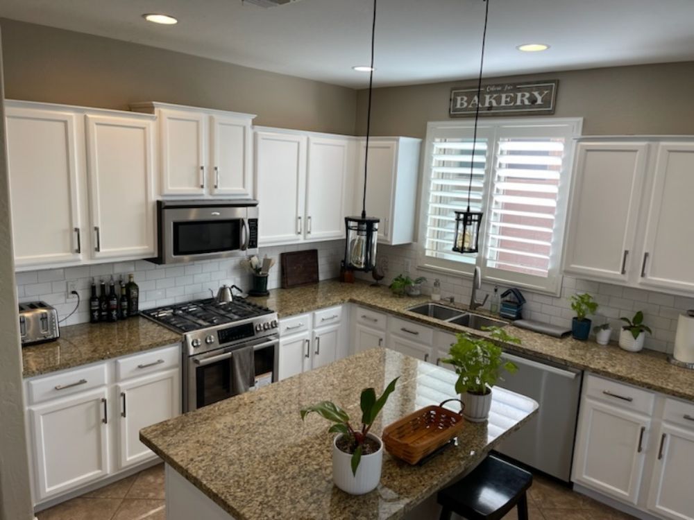 A kitchen with white cabinets , granite counter tops , stainless steel appliances and a sign that says bakery.