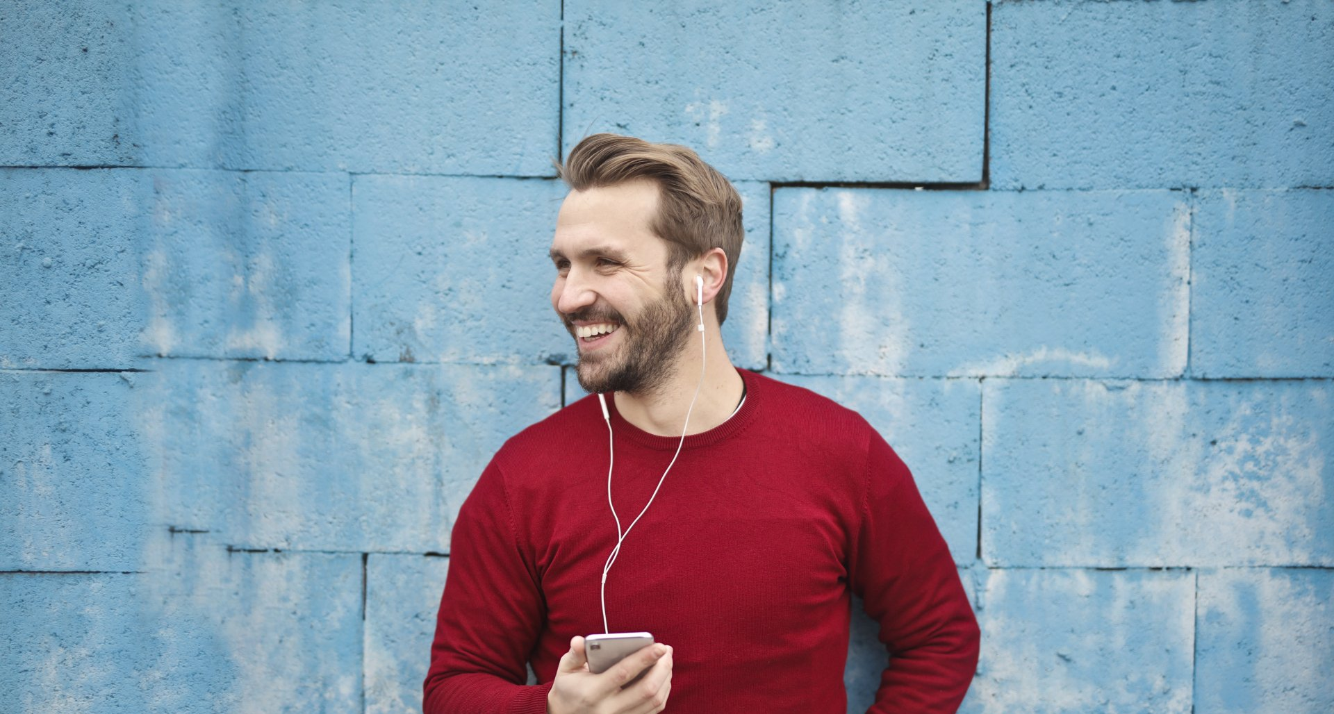 Woman with brown hair swirling in a forest, wearing a burgundy sweater and jeans, sunlight filtering through trees.