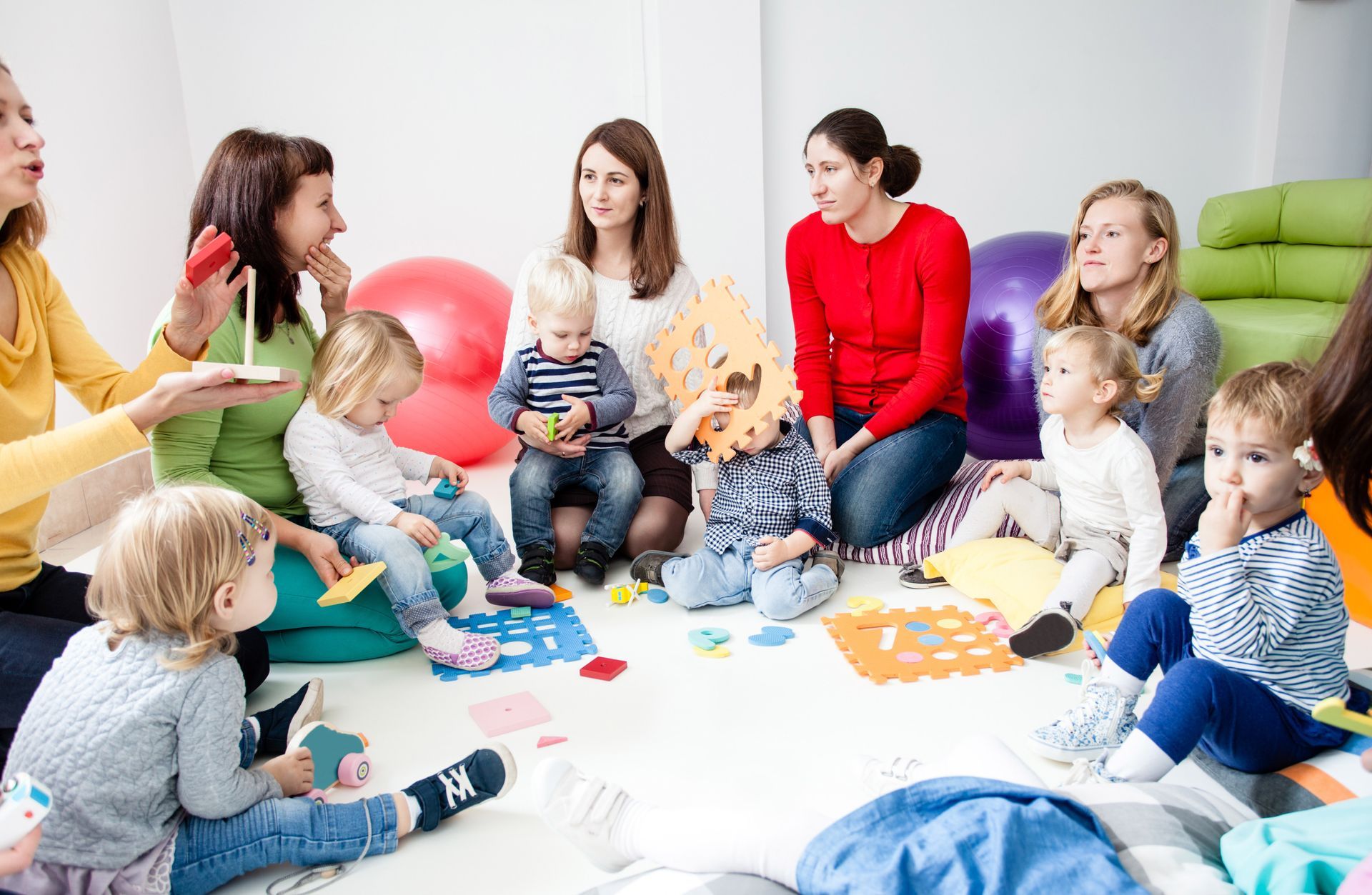 Group of women and children in a circle; activity with toys and a presenter.
